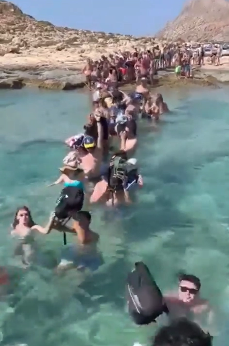 Kreta: Touristen waten mit Gepäck durch das Meer