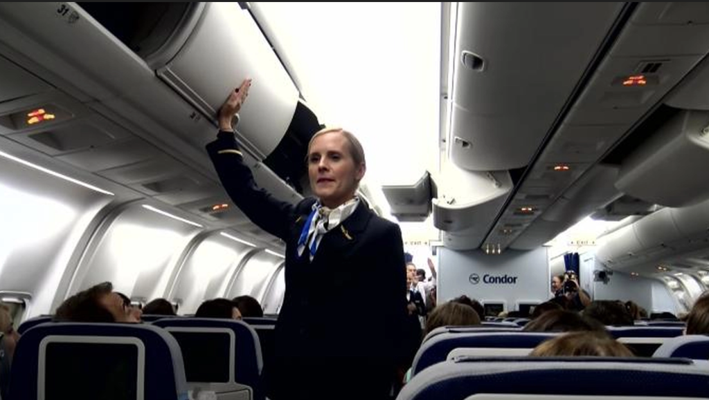 Stewardess klopft an Gepäckfach und Passagiere erleben die Überraschung ihres Lebens
